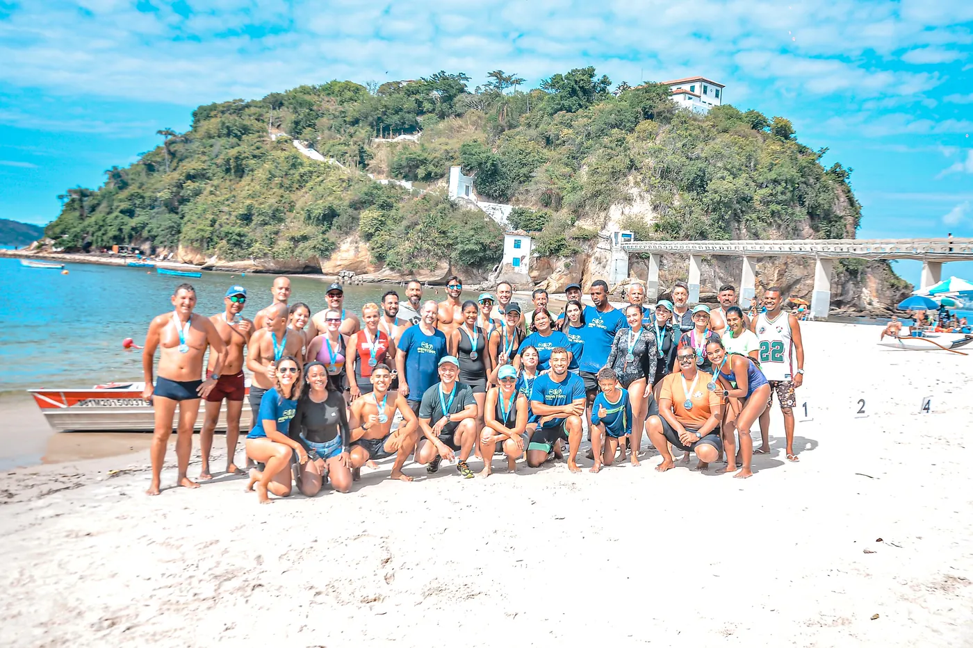 Turma da Papa Tempo reunida na Praia da Boa Viagem com medalhas, com a Ilha da Boa Viagem ao fundo